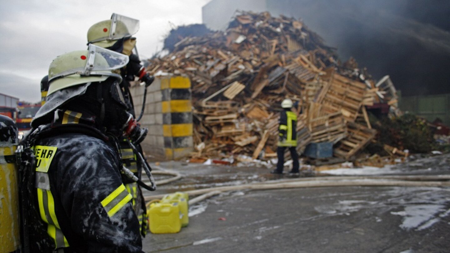 Zwei Feuerwehrleute mit Atemschutzmaske vor einem zerstörten Gebäude