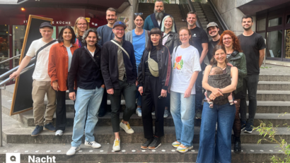 Bei dem Foto handelt es sich um ein Gruppenbild, das 16 Personen zeigt, die auf einer Treppe stehen und alle in die Kamera schauen.