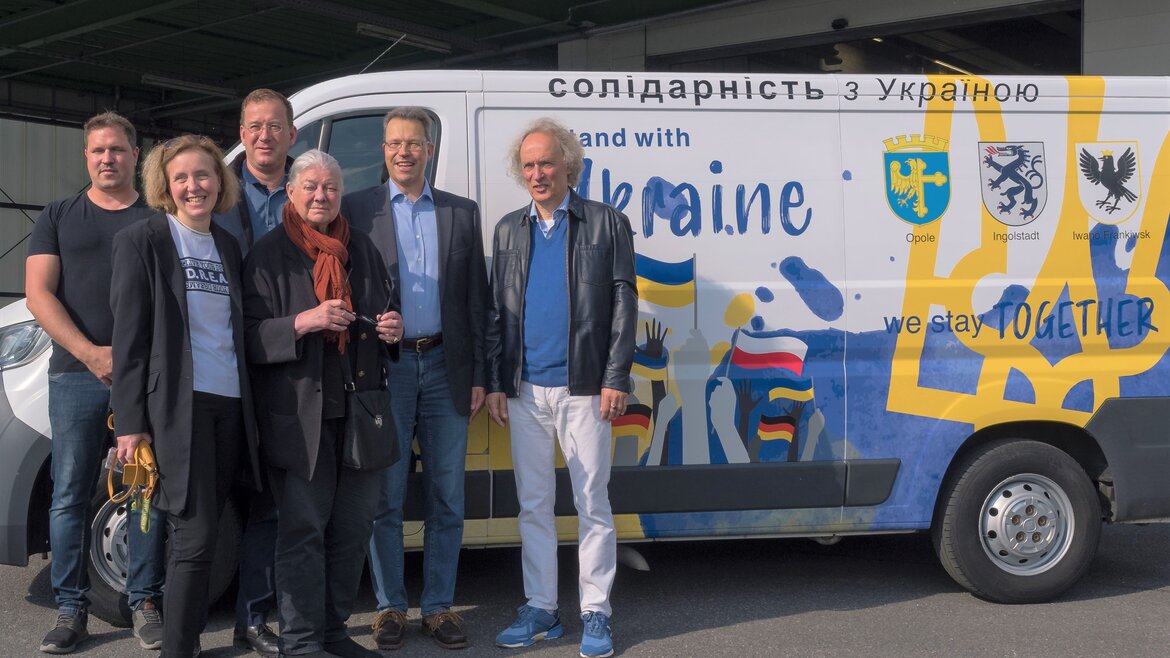 Mehrere Personen stehen vor einem Van mit der Aufschrift "Stand with Ukraine"