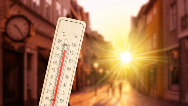 Ein Thermometer vor einer sonnendurchfluteten Straße zeigt hohe Temperaturen an.