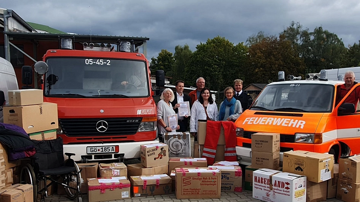 Eine Gruppe an Menschen steht zwischen zwei Feuerwehrfahrzeugen und vor gepackten Kartons