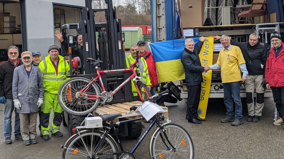 Eine Gruppe von Menschen steht vor einer Ukraine-Flagge und zwei Fahrrädern