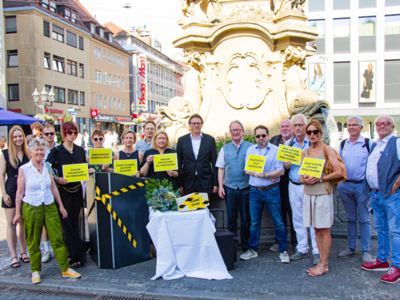 Oberbürgermeister Martin Heilig (Mitte) in Würzburg, 2. Bürgermeisterin Dr. Sandra Vorlová (links neben dem OB), 3. Bürgermeister Joachim Spatz (rechts neben dem OB) und Kämmerin Beate Gross (mit dem Schild "Leere Kassen, kaputte Klassen") zusammen mit Stadträtinnen und Stadträten.