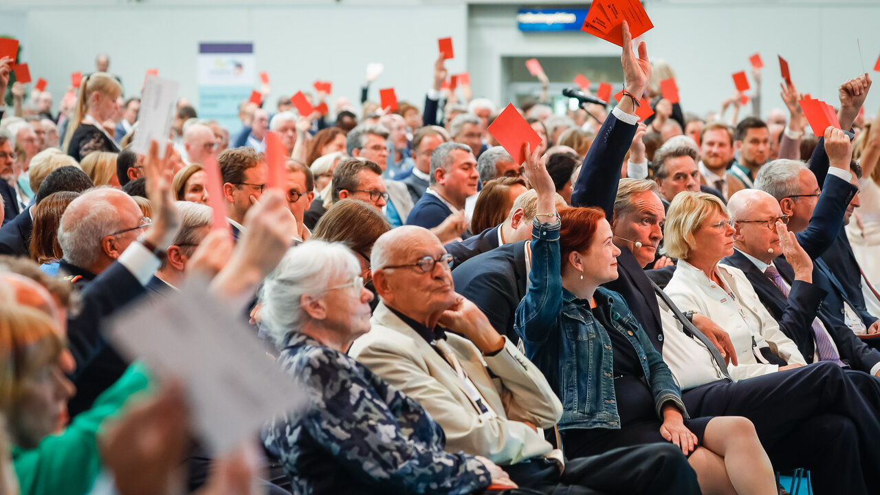 Teilnehmende halten während einer Abstimmung rote Wahlkarten nach oben.