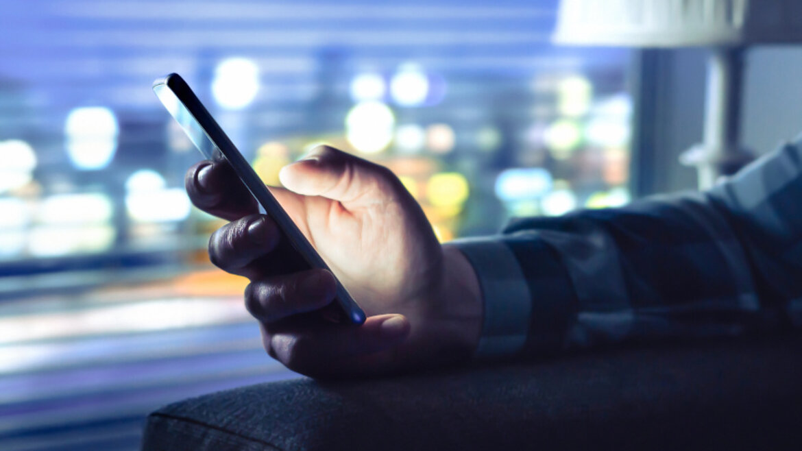 Person hält Smartphone in abgedunkeltem Raum in der Hand.