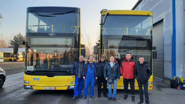 Eine Gruppe von Menschen steht vor zwei Linienbussen