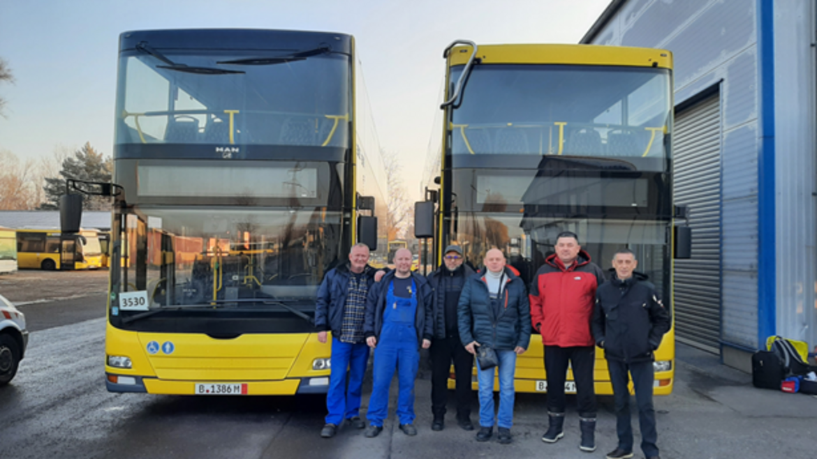 Eine Gruppe von Menschen steht vor zwei Linienbussen
