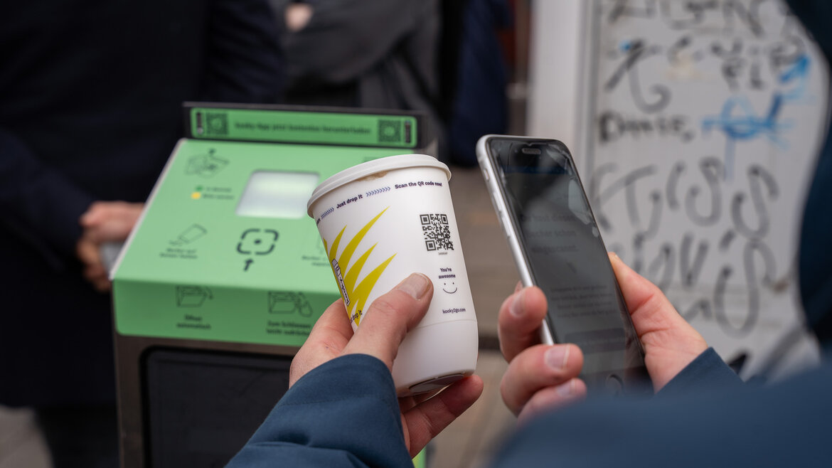 QR-Code auf einem Mehrweg-To-Go-Becher wird vor dem Einwerfen in eine Rückgabesäule mit dem Handy gescannt.