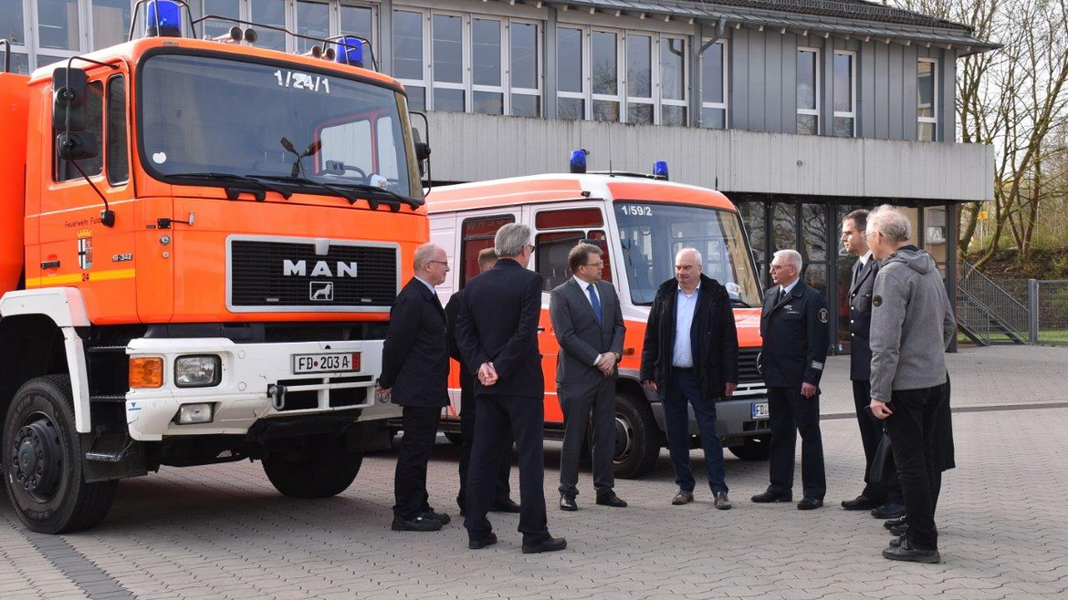 Eine Gruppe von Menschen steht vor zwei Feuerwehrfahrzeugen