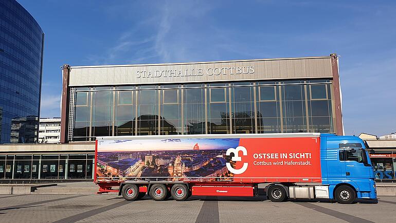 LKW mit Auflieger, auf dem "Ostsee in Sicht! Cottbus wird Hafenstadt" steht, parkt vor der Stadthalle Cottbus