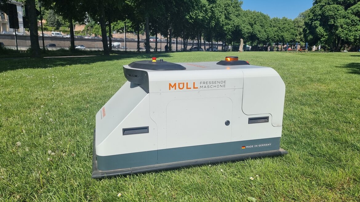 Roboter mit Aufschrift "Müll fressende Maschine" auf einer Grasfläche