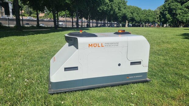 Roboter mit Aufschrift "Müll fressende Maschine" auf einer Grasfläche