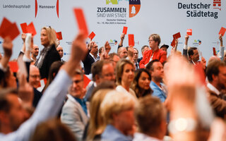 Teilnehmende halten während einer Abstimmung rote Wahlkarten nach oben.