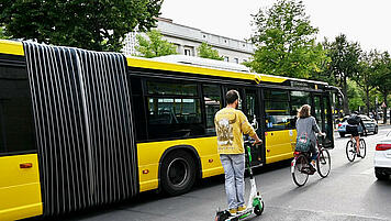 Bus, Scooter, Fahrradfahrer und parkendes Auto im Straßenverkehr