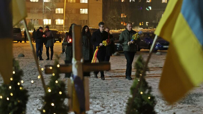 Zwei Männer legen Kränze nieder, im Vordergrund weht eine ukrainische Flagge.