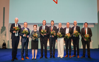 Wolfram Leibe, Frank Nopper, Katja Dörner, Burkhard Jung, Uwe Conradt, Sibylle Keupen, Eckart Würzner, Belit Onay und André Stahl stehen für ein Gruppenfoto auf einer Bühne und halten Blumensträuße.
