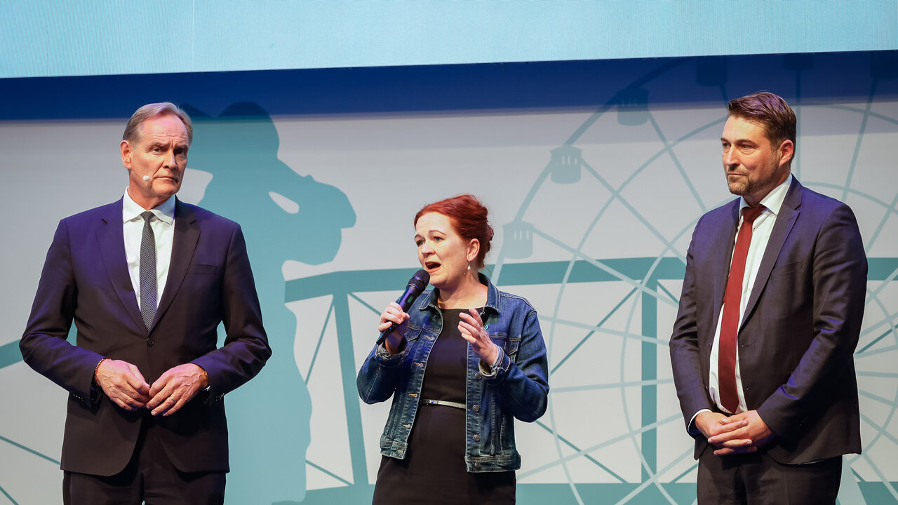 Burkhard Jung, Katja Dörner und Uwe Conradt stehen auf einer Bühne, Dörner spricht in ein Mikrofon.